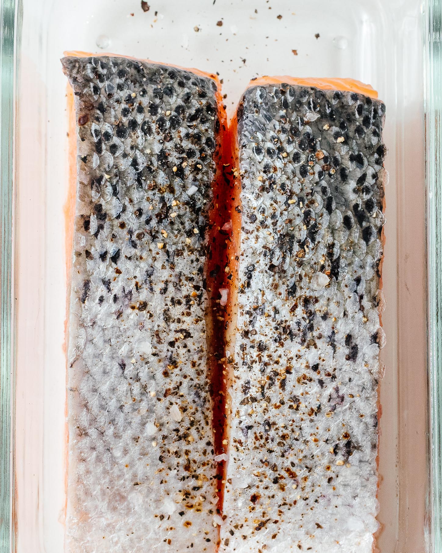 Two pink salmon fillets, skin side up and speckled with pepper, ready to cook