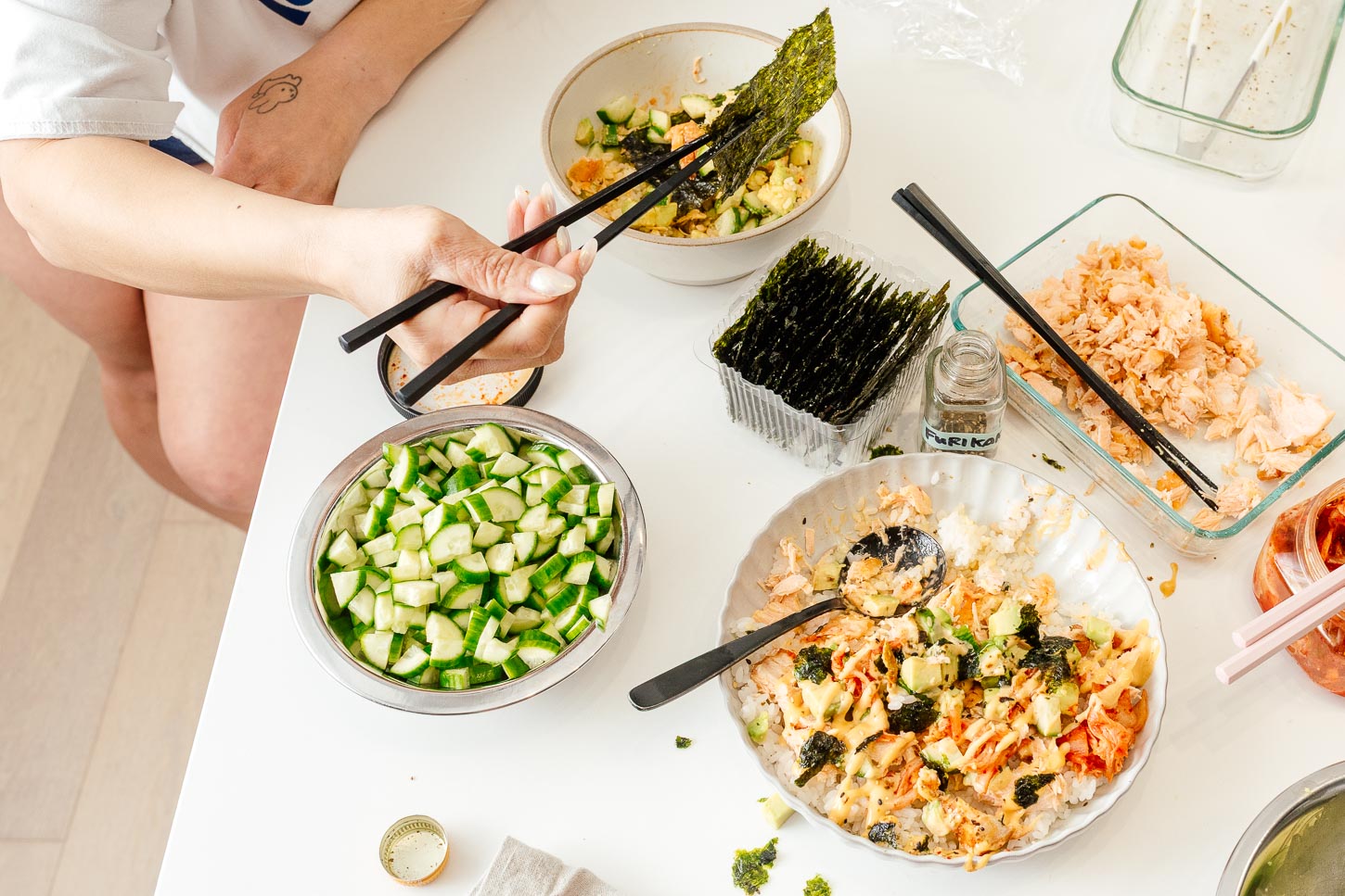 Digging into a salmon rice bowl with chopsticks and seaweed snacks, crunchy cucumbers and kimchi on the side